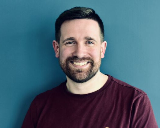 Professional photo of Daniel (a white, bearded man in his early 40s) smiling into the camera