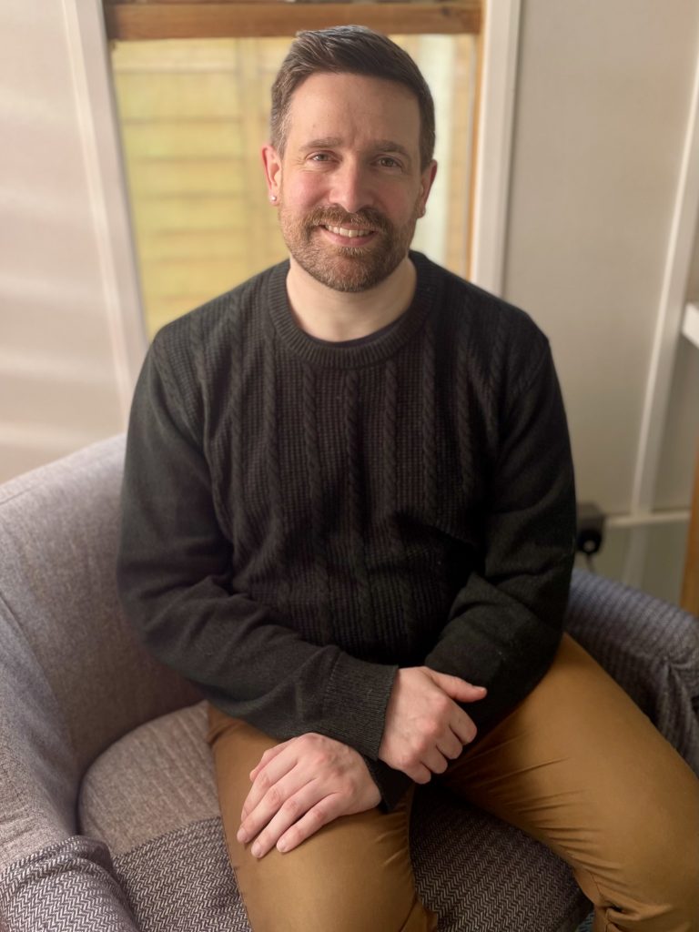 Photgraph of Daniel Winstanley, seated in his counselling room. He is smiling.